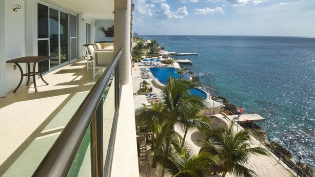 Un balcón con vistas al océano, una piscina y sillas de playa.