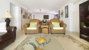 Amplia sala de estar con dos sillones de mimbre, un sofá de cuero marrón y una mesa de centro de vidrio.