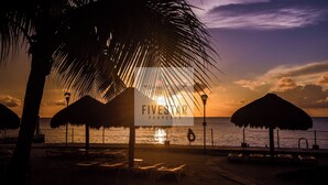 Escena de playa con atardecer, palmeras y un letrero de Fivesmar Property.