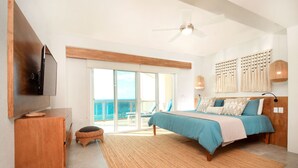 Una camera da letto con un letto, una televisione, una ventola a soffitto, un'ampia finestra e vista sull'oceano.