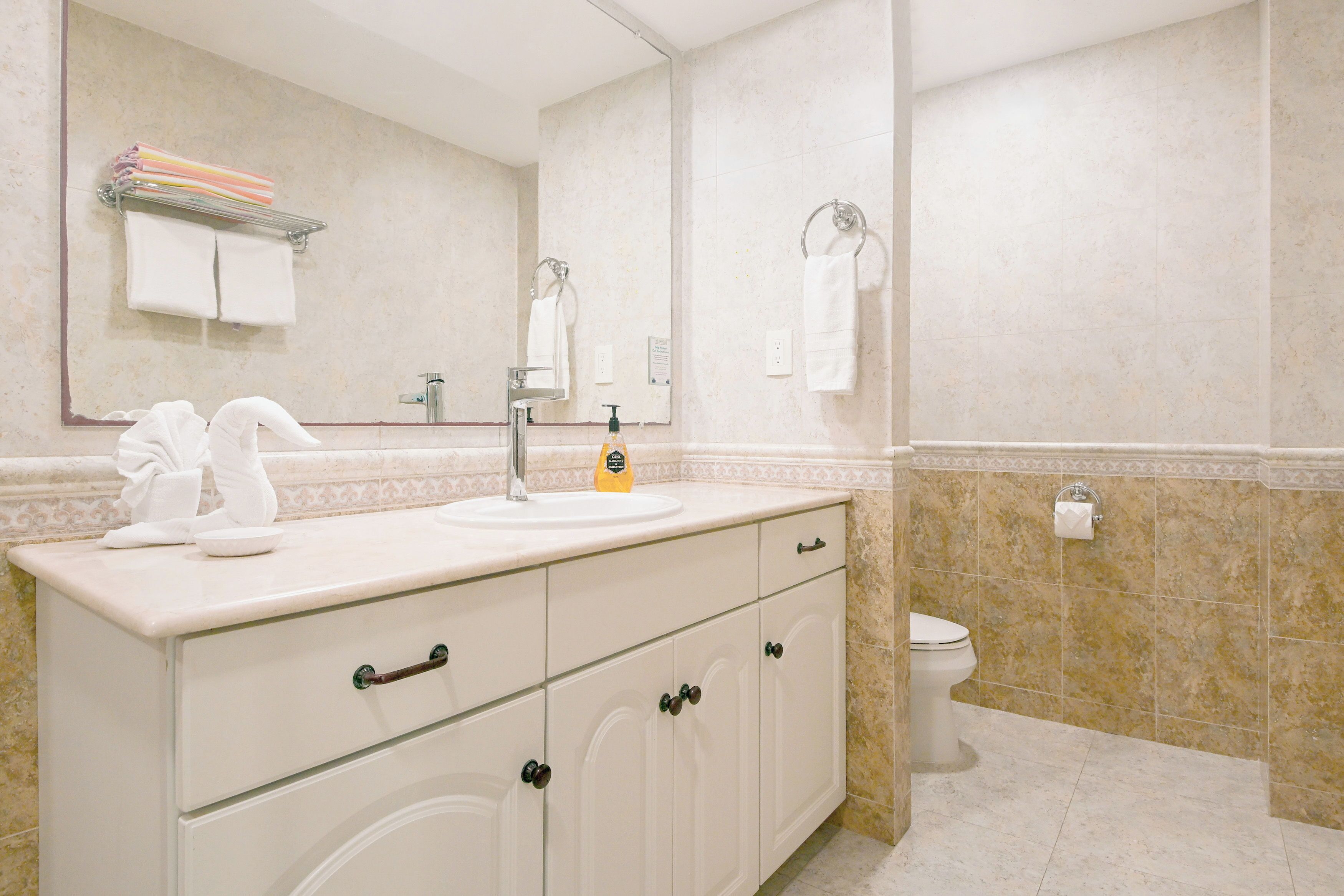 A bathroom with a white vanity, a sink, a mirror, a toilet, and a towel rack.