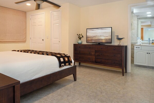 Un dormitorio con cama, cómoda, televisor y baño visible a través de una puerta abierta.