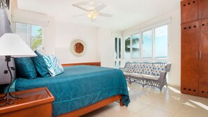 Une chambre à coucher avec un lit, une table de chevet, un ventilateur de plafond, une fenêtre et une vue sur des palmiers.