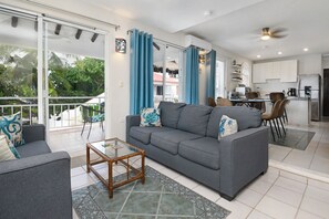 A modern living room with a grey sofa, a glass coffee table, and a view of the outdoor balcony. - Diver's Paradise!  3 Bdrm True Oceanfront! 2A (San Miguel de Cozumel)