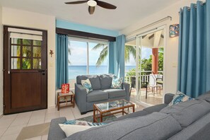 A living room with a view of the ocean, a ceiling fan, and a sliding glass door leading to an outdoor area. - Diver's Paradise!  3 Bdrm True Oceanfront! 2A (San Miguel de Cozumel)