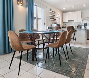 Een eetruimte met een ronde tafel, zes stoelen en een keuken op de achtergrond.