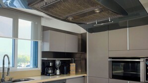 A modern kitchen with a black induction cooktop, stainless steel appliances, and a large window providing natural light.