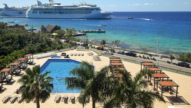 Un resort con piscina, sillas de playa y vistas al océano y cruceros.