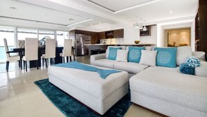 Una sala de estar moderna con un sofá modular, un comedor con sillas y una cocina al fondo.