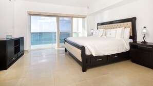 Un dormitorio con una cama grande, una mesita de noche, un aparador y un ventanal corredero que da a un balcón con vistas al mar.