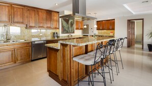 A kitchen with wooden cabinets, a stainless steel range hood, granite countertops, and a bar area with stools.