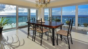 A dining area with a large table and chairs, large windows with ocean views, and a chandelier.