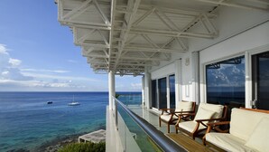 A balcony with a view of the ocean and boats, featuring white railings and wooden chairs.