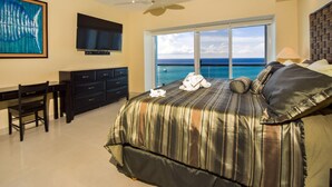 A bedroom with a large bed, a desk, a television, and a view of the ocean.