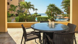 Una mesa redonda de cristal con cuatro sillas, un jarrón pequeño y vistas a una piscina y una playa.