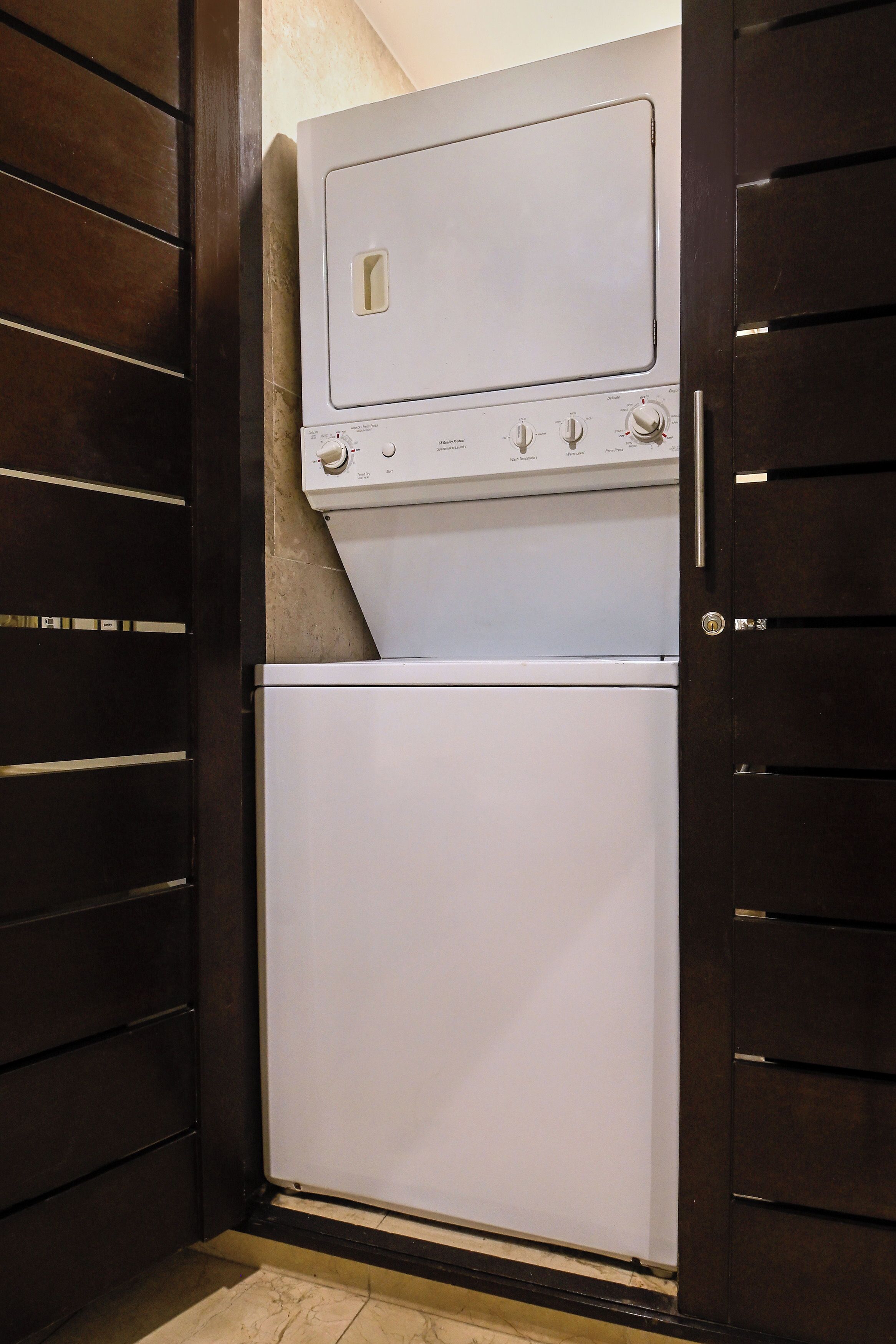 A compact laundry room with a washer and dryer, dark wooden doors, and tiled flooring.