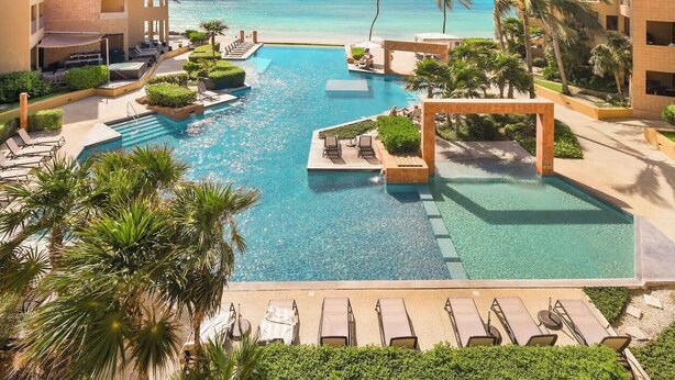 A resort pool area with multiple swimming pools, lounge chairs, and palm trees.
