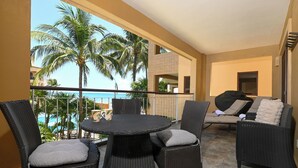 A balcony with wicker furniture, a view of palm trees, and a pool.