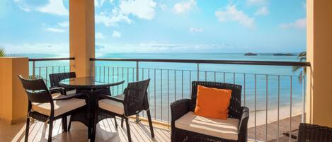Een balkon met een tafel en stoelen, met uitzicht op een heldere blauwe zee en een eiland in de verte.