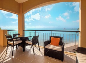 A balcony with a table and chairs, overlooking a clear blue sea and a distant island.