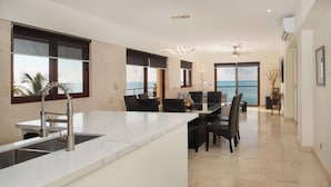 Eine moderne Küche mit einer großen Kochinsel, ein Essbereich mit Meerblick und ein Balkon mit Ausblick aufs Meer.