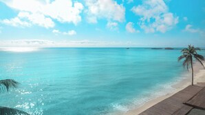 Ein Strand mit klarem türkisblauem Wasser, einer Holzpromenade und einer Palme.