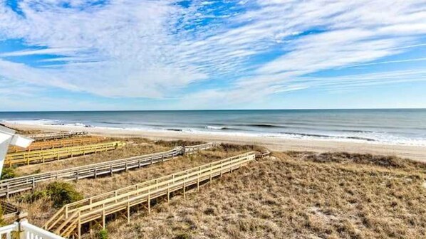 A beach with wooden boardwalks leading to the shore, a clear sky, and calm ocean waves.