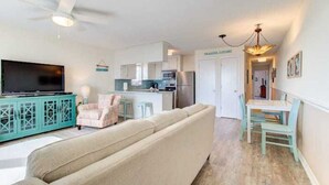 Una sala de estar moderna con un sofá, un televisor y una cocina con refrigerador y microondas.