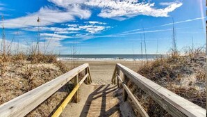 Un paseo marítimo de madera que conduce a una playa, con el océano al fondo.