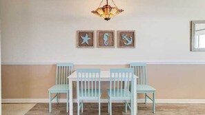 A dining area with a white table and light blue chairs, a chandelier, and three wall art pieces depicting sea creatures.