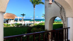 Vista a través de un arco de un resort de playa con piscina, palmeras y cielo azul despejado.