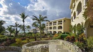 Un patio con paredes de piedra, palmeras y un edificio con varios balcones y arcos.