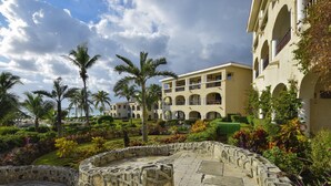 A courtyard with stone walls, palm trees, and a building with multiple balconies and arches.
