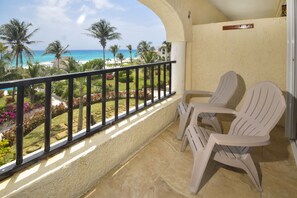 A balcony with a view of the beach, two white chairs, and a sign indicating a room number.