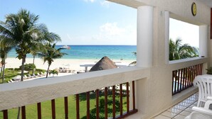 Un balcon avec vue sur une plage, des palmiers et une construction à toit de chaume.