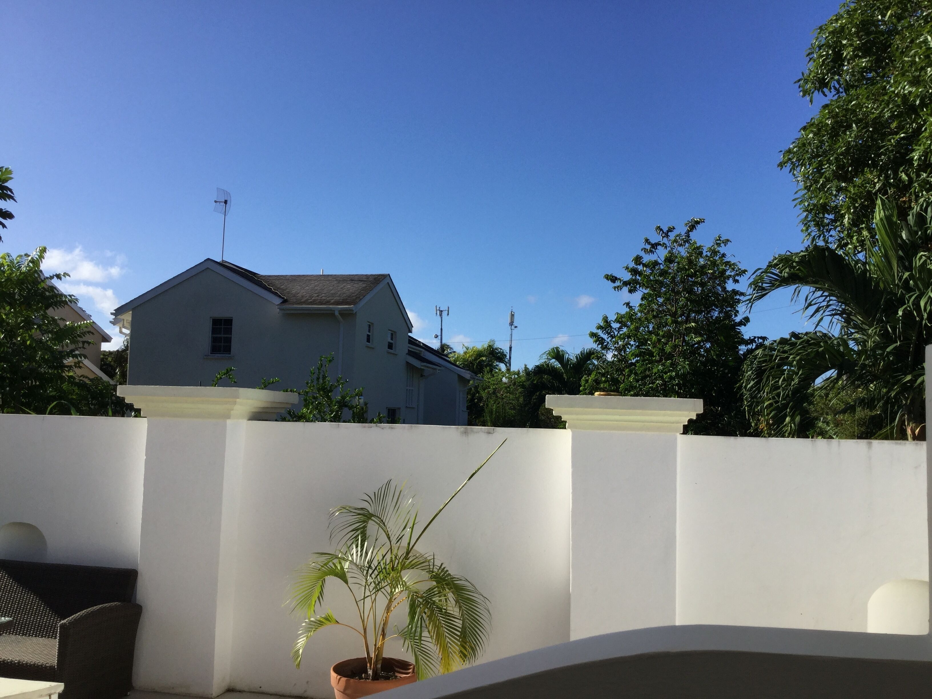 Et hvidt hus med et gråt tag, omgivet af grøn vegetation og en hvid mur.