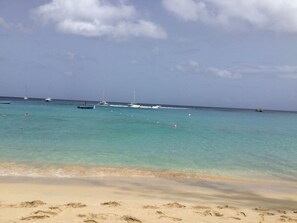 A beach with clear turquoise water, boats, and footprints on the sand.