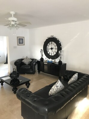 A modern living room with a black leather sofa, a black coffee table, a black sideboard, and a large wall clock.