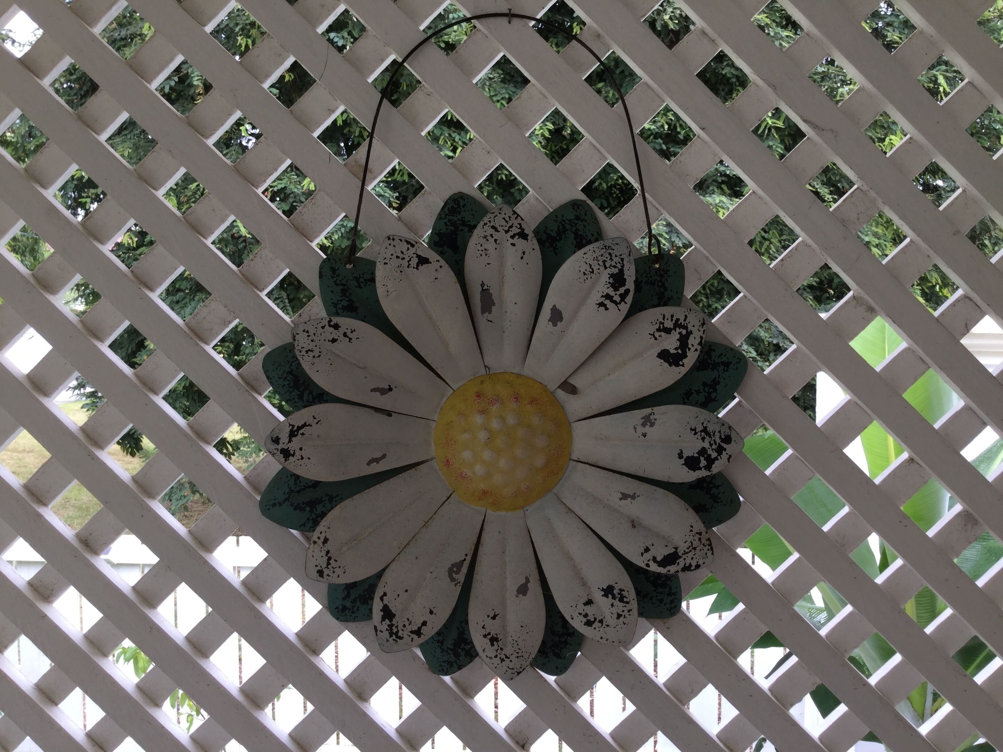 A decorative flower with a yellow center and white petals with green accents, set against a white lattice background.