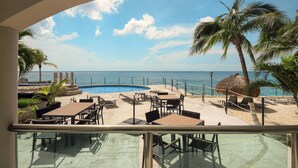 A poolside area with tables and chairs, a thatched umbrella, and a view of the ocean. - Ground Floor 2 Bdrm Ocean Views! El Cantil LBN (San Miguel de Cozumel)