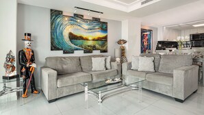 A modern living room with two grey sofas, a glass coffee table, and a large abstract painting. - Ground Floor 2 Bdrm Ocean Views! El Cantil LBN (San Miguel de Cozumel)
