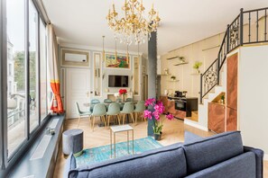 A spacious living area with a modern chandelier, a dining set, and a kitchen with a staircase. - Merveil - Luxury Suite - Louvre - Reaumur I (Paris)