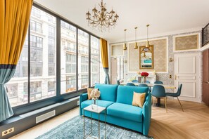 Una sala de estar moderna con un sofá azul, un comedor con sillas azules y un amplio ventanal con cortinas.