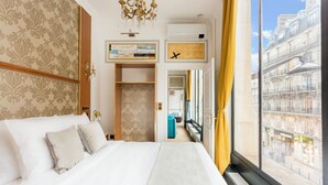 A hotel room with a large bed, a wardrobe, a desk, and a view of the city.