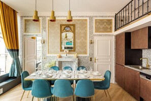 Un comedor con chimenea de mármol, espejos con marco dorado y sillas color turquesa.