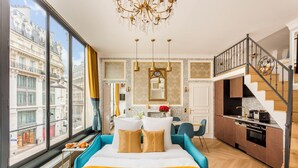 A modern hotel room with a large bed, a dining area, and a kitchen.
