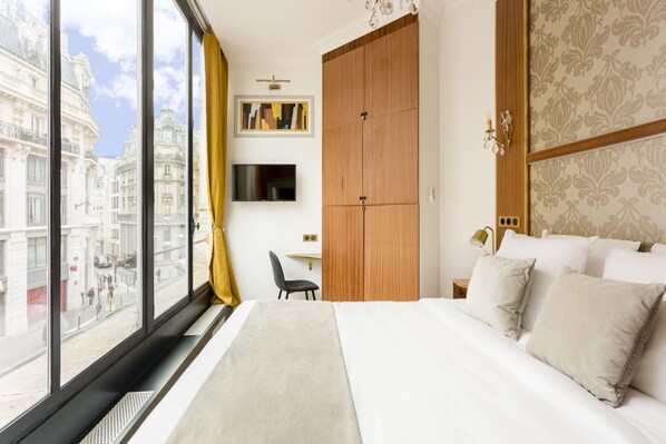 A hotel room with a large bed, a desk, a TV, and a wardrobe.