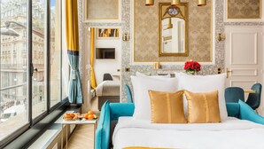 A hotel room with a large bed, a view of the city, a television, and a dining area with breakfast.