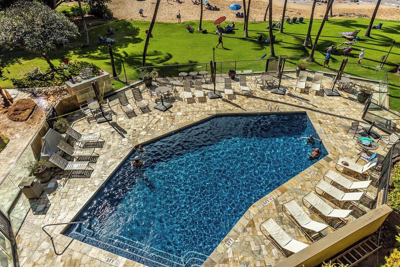 Piscina com espreguiçadeiras e área gramada com guarda-sóis.