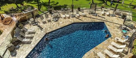 Piscina com espreguiçadeiras e área gramada com guarda-sóis.